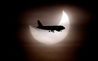 An aeroplane is silhouetted against a partial solar eclipse as seen in the cloudy skies over Barcelona, Spain